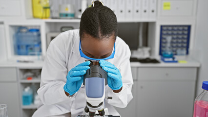 Focused african american woman scientist engrossed in scientific research, on microscope analysis...