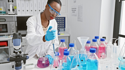 Black beauty in lab goggles, focused african american woman scientist firmly holds test tube, pouring liquid meticulously in bustling medical laboratory deep in concentration. - obrazy, fototapety, plakaty