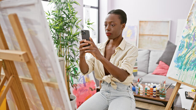Confident african american woman artist draws beautiful art in studio using a smartphone to make reference picture