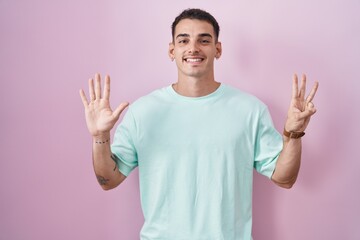 Naklejka premium Handsome hispanic man standing over pink background showing and pointing up with fingers number eight while smiling confident and happy.