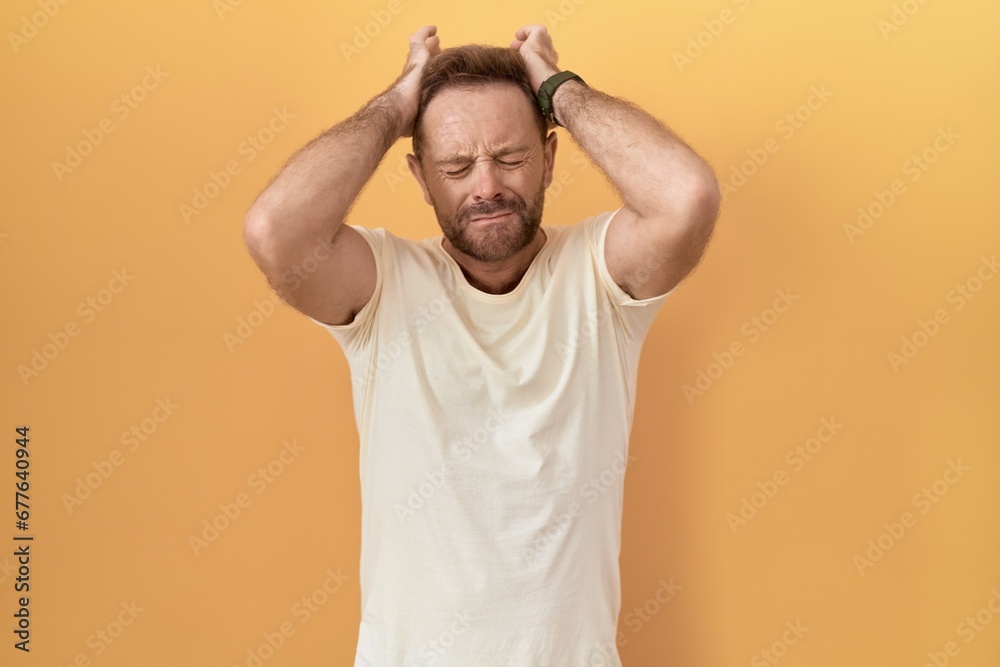 Poster Middle age man with beard standing over yellow background suffering from headache desperate and stressed because pain and migraine. hands on head.