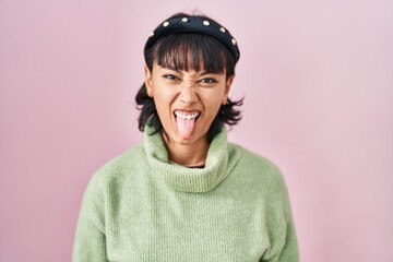 Young beautiful woman standing over pink background sticking tongue out happy with funny expression. emotion concept.