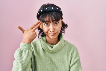Young beautiful woman standing over pink background shooting and killing oneself pointing hand and fingers to head like gun, suicide gesture.