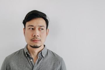 Close up of Asian man with beard wear grey t-shirt emotionless face, looking at empty space isolated over white background wall.