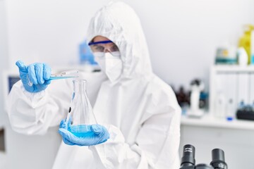 Fototapeta premium Young blonde woman scientist wearing security uniform pouring liquid on test tube at laboratory