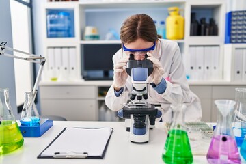 Young blonde woman scientist using microscope at laboratory