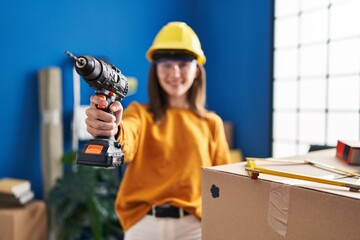 Young blonde woman wearing hardhat holding drill at new home