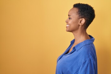 African american woman standing over yellow background looking to side, relax profile pose with...
