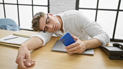 Exhausted young caucasian businessman, smartphone in hand, loses battle with stressâ€“ nobly...