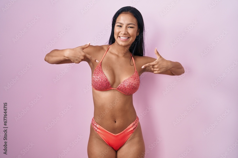 Wall mural hispanic woman wearing bikini looking confident with smile on face, pointing oneself with fingers pr