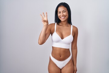 Hispanic woman wearing lingerie showing and pointing up with fingers number three while smiling...