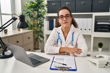 Young hispanic woman wearing doctor uniform and stethoscope relaxed with serious expression on face. simple and natural looking at the camera.