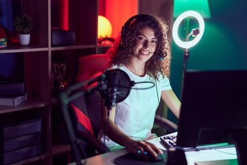 Young beautiful hispanic woman streamer playing video game using computer at gaming room