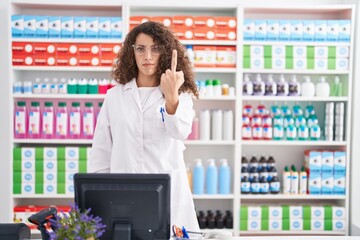 Hispanic woman with curly hair working at pharmacy drugstore showing middle finger, impolite and...