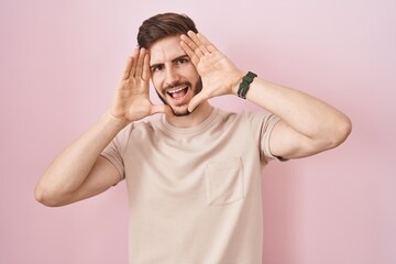 Hispanic man with beard standing over pink background smiling cheerful playing peek a boo with...
