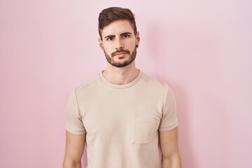 Hispanic man with beard standing over pink background relaxed with serious expression on face. simple and natural looking at the camera.
