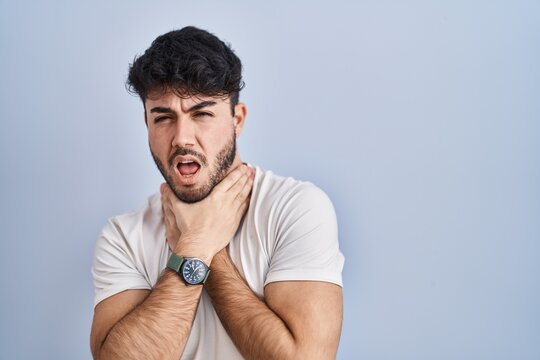 Hispanic man with beard standing over white background shouting suffocate because painful strangle. health problem. asphyxiate and suicide concept.