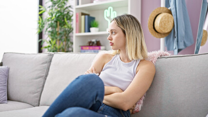 Young blonde woman sitting on sofa with arms crossed gesture and serious face at home