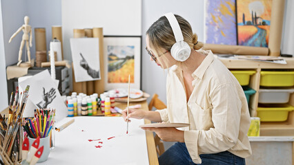 Fototapeta na wymiar Young blonde woman artist drawing on paper listening to music at art studio