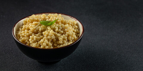 Ptitim or Birdy, Israeli pasta couscous in a bowl on a dark background, Long banner format. top view. copy space for text