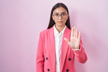 Young hispanic woman wearing business clothes and glasses doing stop sing with palm of the hand. warning expression with negative and serious gesture on the face.