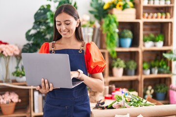 Young beautiful hispanic woman florist smiling confident using laptop at florist