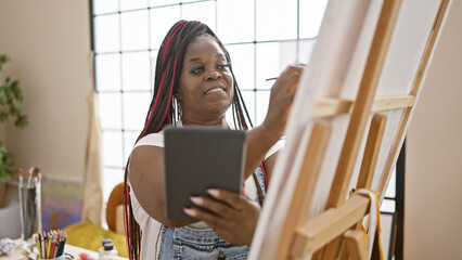 Confident, beautiful african american woman artist happily drawing on touchpad, bringing creativity to life in modern art studio setting.