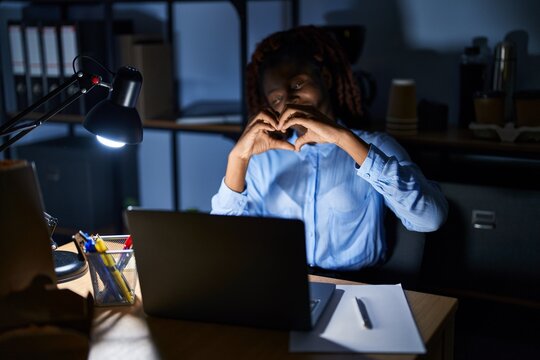 African woman working at the office at night smiling in love doing heart symbol shape with hands. romantic concept.