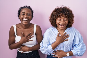 Two african women standing over pink background smiling and laughing hard out loud because funny...