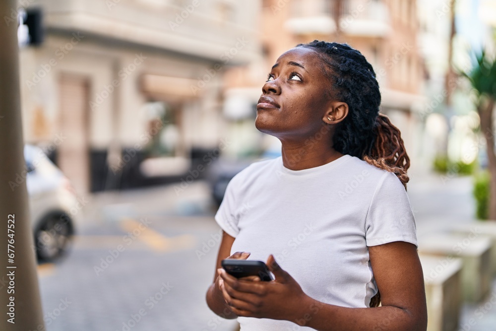 Wall mural African american woman using smartphone with worried expression at street