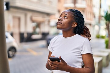 African american woman using smartphone with worried expression at street