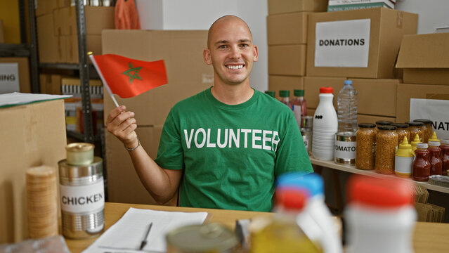 Young hispanic man volunteer smiling confident holding morocco flag at charity center