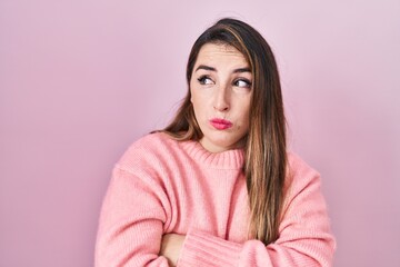 Fototapeta premium Young hispanic woman standing over pink background looking to the side with arms crossed convinced and confident