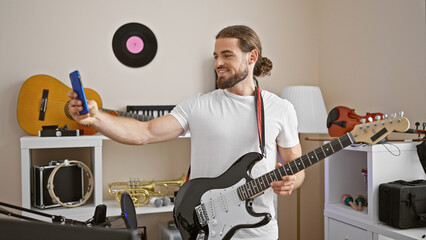 Young hispanic man musician playing electrical guitar make selfie by smartphone at music studio