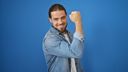 Fototapeta premium Young hispanic man smiling confident doing strong gesture with arm over isolated blue background