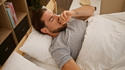 Obraz na płótnie Canvas Young hispanic man lying on bed yawning at bedroom