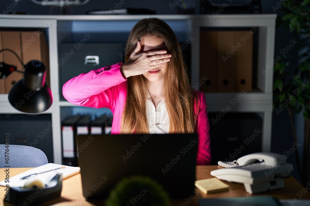 Canvas Prints Young caucasian woman working at the office at night smiling and laughing with hand on face covering eyes for surprise. blind concept.