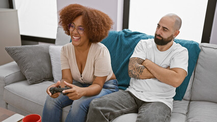 Beautiful interracial couple, looking upset, sit together at home playing video game - love...