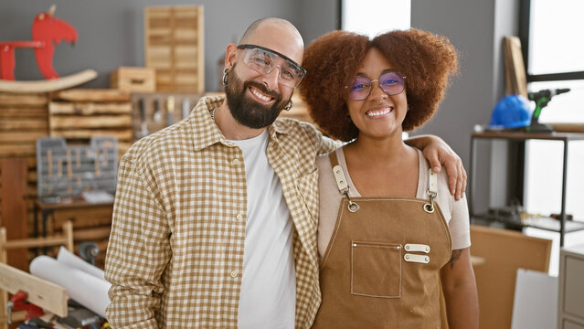 Two smiling carpenters in safety glasses, hugging amid the lumber, together, bringing joy to the carpentry industry