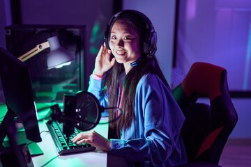 Young chinese woman streamer playing video game using computer at gaming room