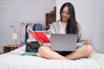 Young chinese woman using laptop reading notebook studying on bed at bedroom