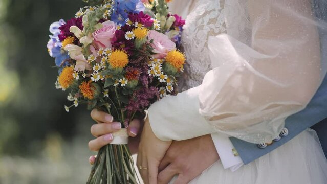 Close-up shot of a couple holding bouquets in their hands while hugging each other - wedding bouquet of fresh rose lupine and other flowers of pink and violet colors