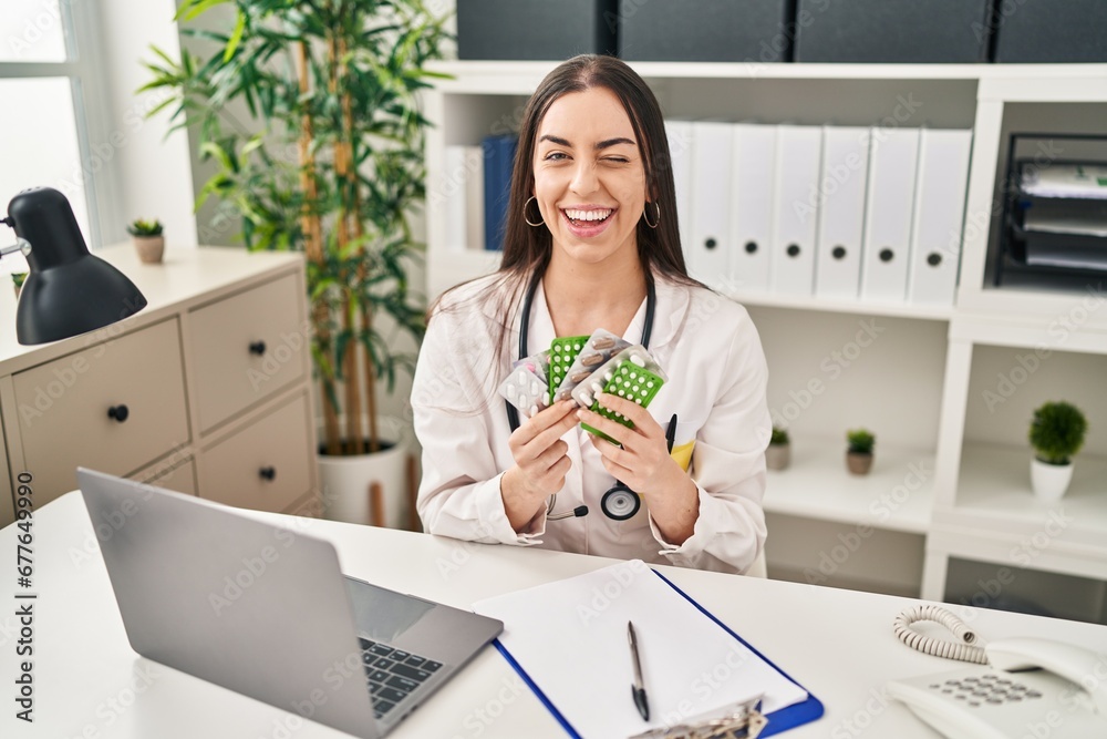 Canvas Prints Hispanic doctor woman holding prescription pills winking looking at the camera with sexy expression, cheerful and happy face.