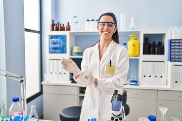 Young beautiful hispanic woman scientist smiling confident wearing gloves at laboratory