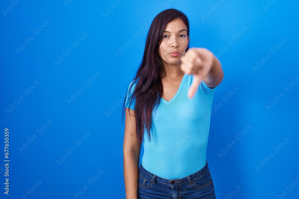 Sticker young hispanic woman standing over blue background looking unhappy and angry showing rejection and n