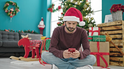 Young hispanic man using smartphone celebrating christmas at home