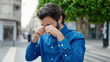 Young hispanic man rubbing the eyes at street