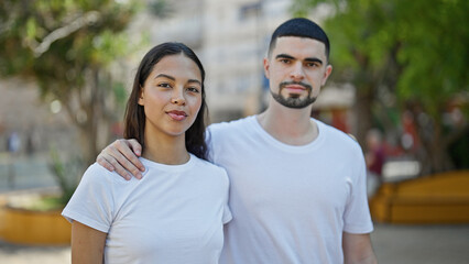 Obraz premium Beautiful, serious-faced couple deeply hugging each other in a green city park, expressive outdoor love between two lovely people living a relaxed, casual lifestyle, basking in sunny nature