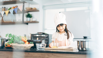 Little asian girl with chef hat and apron cooking at home kitchen