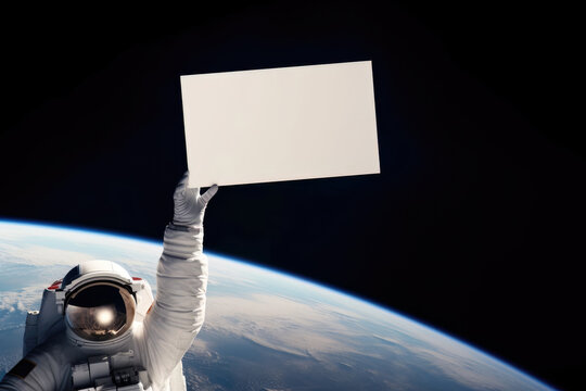 Astronaut in outer space holding a blank sign in his hand, in background planet earth